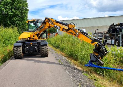 Image of a JCB Hydradig wheeled excavator cutting a road verge with a Slanetrac HC180L Excavator Mounted Hedge Cutter attachment