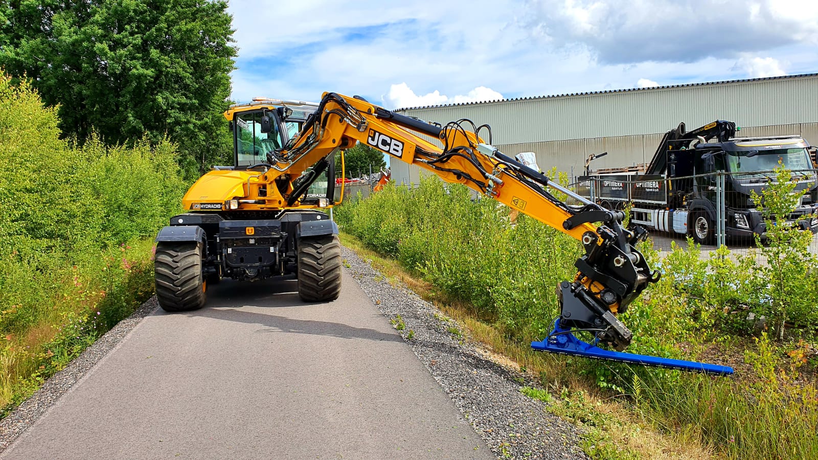 Image of a JCB Hydradig wheeled excavator cutting a road verge with a Slanetrac HC180L Excavator Mounted Hedge Cutter attachment
