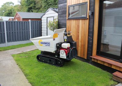 Image of a Chadwicks Slanetrac HT690 The Pup Mini Track Dumper on a lawn area beside a garden room